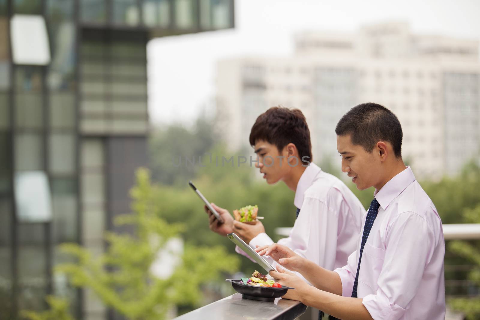 Two young businessmen working outdoor and eating by XiXinXing