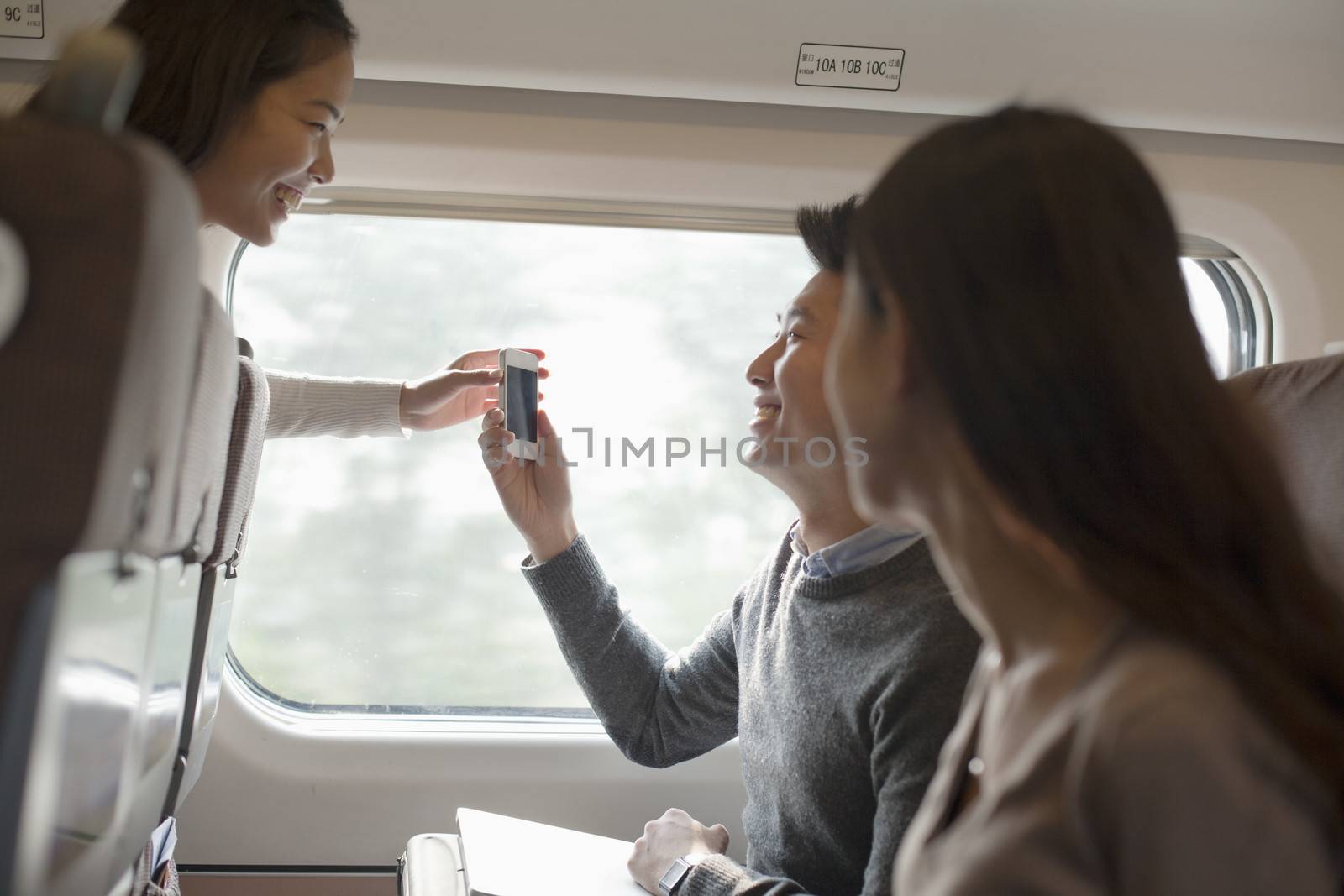 Young man and women using phone on a train, Beijing  by XiXinXing