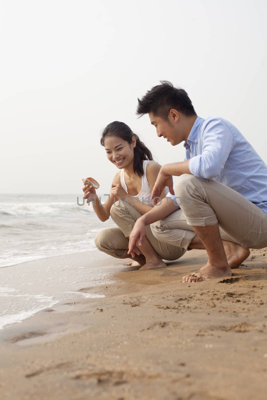 Young couple looking at seashell at the waters edge, China