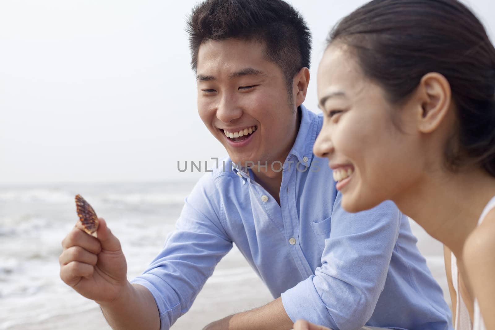 Young couple looking at seashell at the waters edge, China