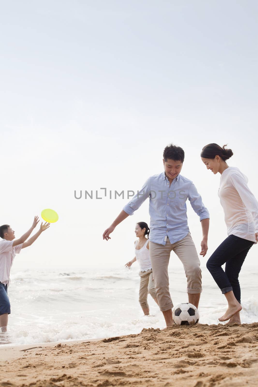 Four young people playing soccer and Frisbee on the beach, China