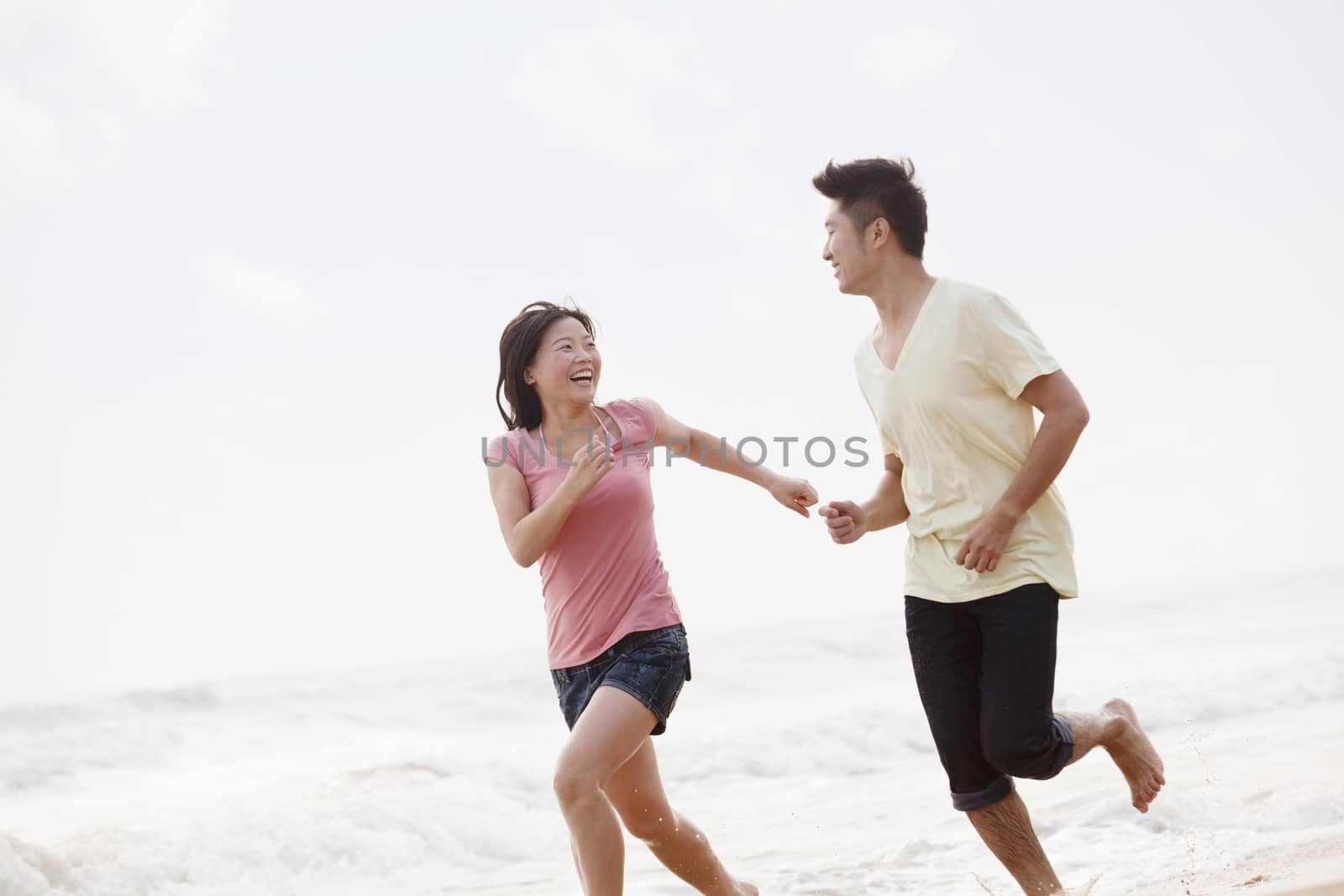 Couple running by the waters edge on the beach, China