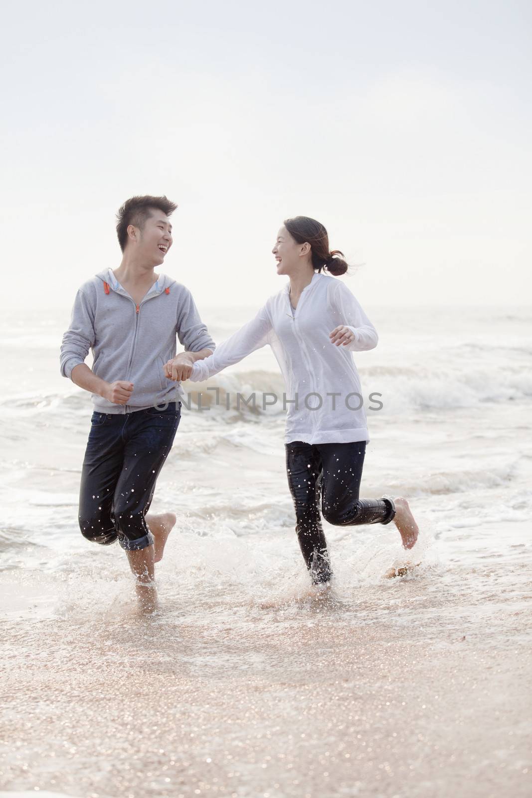 Young couple holding hands and running by the waters edge on the beach, China by XiXinXing