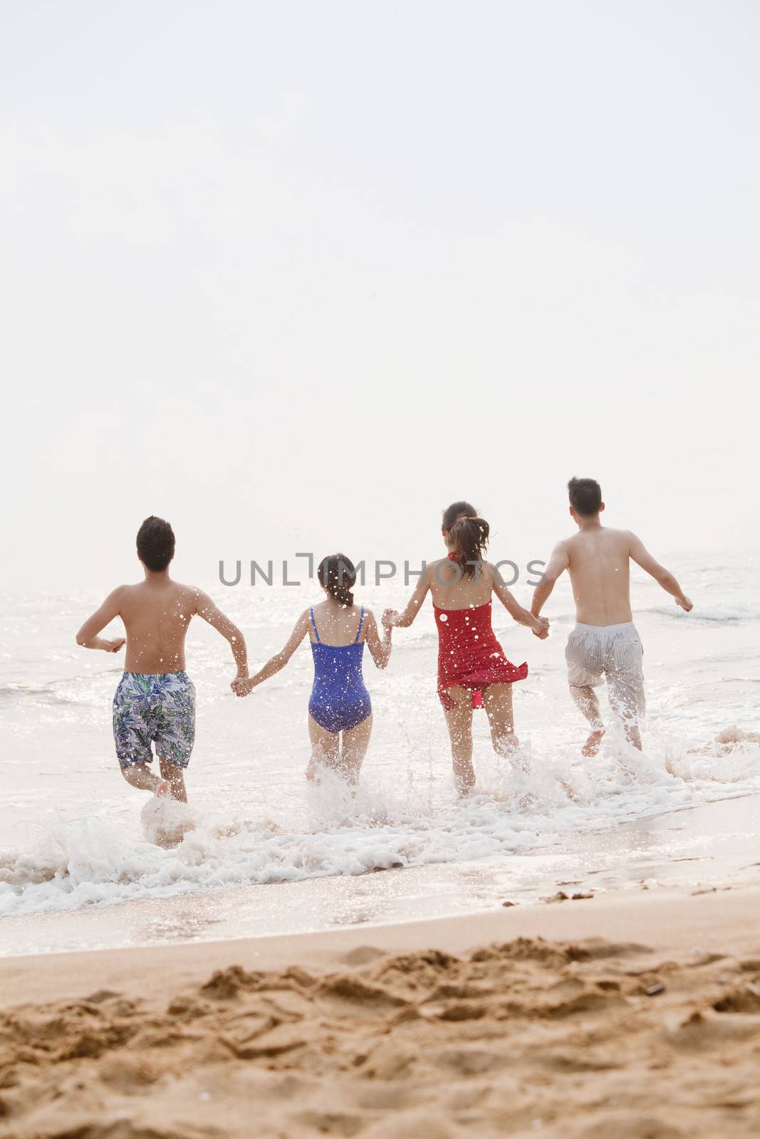 Four friends running into the water on a sandy beach, rear view