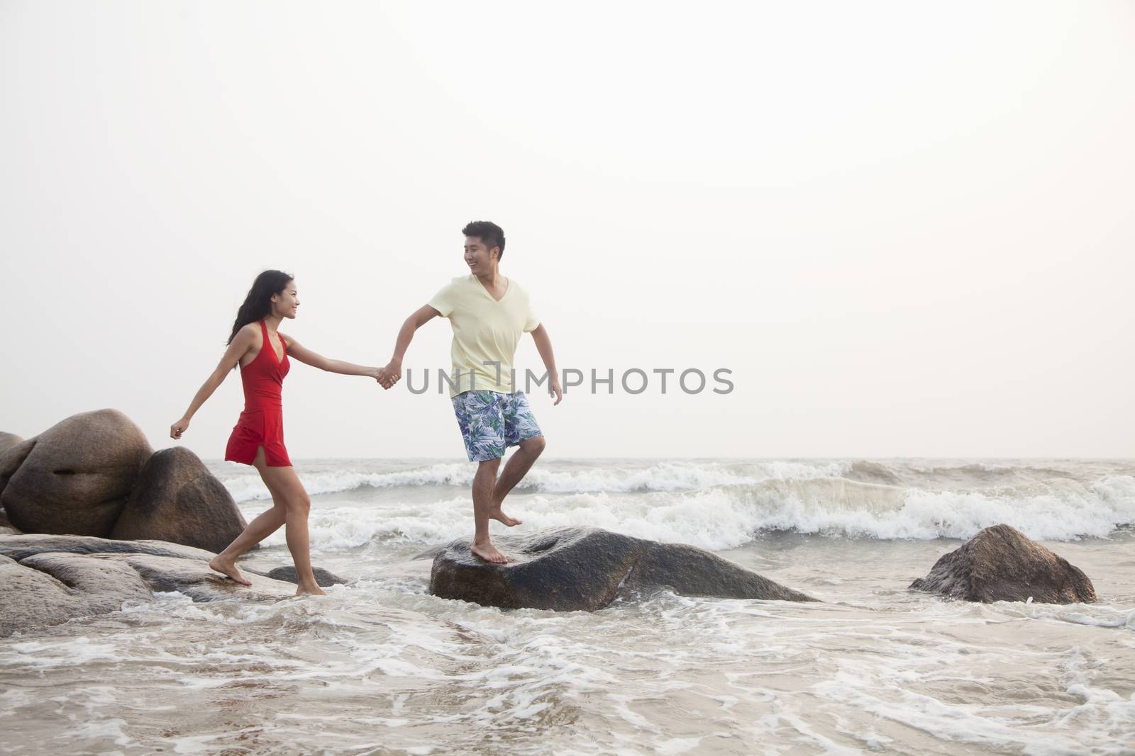 Young couple walking on the beach walking over rocks