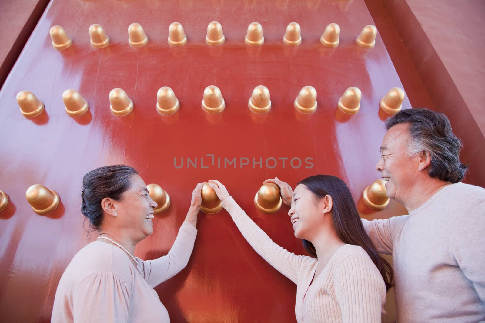 Granddaughter with grandparents standing next to the traditional red doors and holding hands by XiXinXing