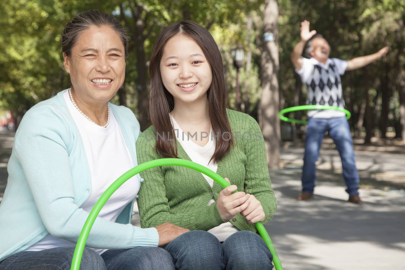 Granddaughter with grandparents playing with plastic hoop in the park by XiXinXing