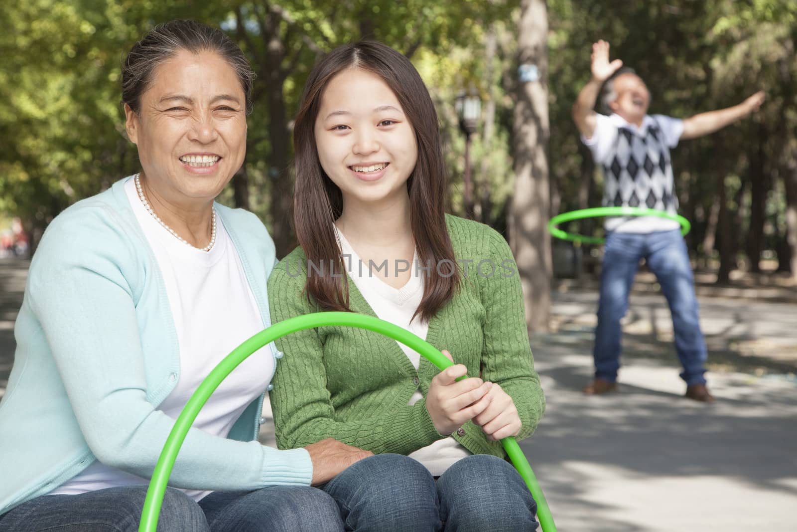 Granddaughter with grandparents playing with plastic hoop in the park