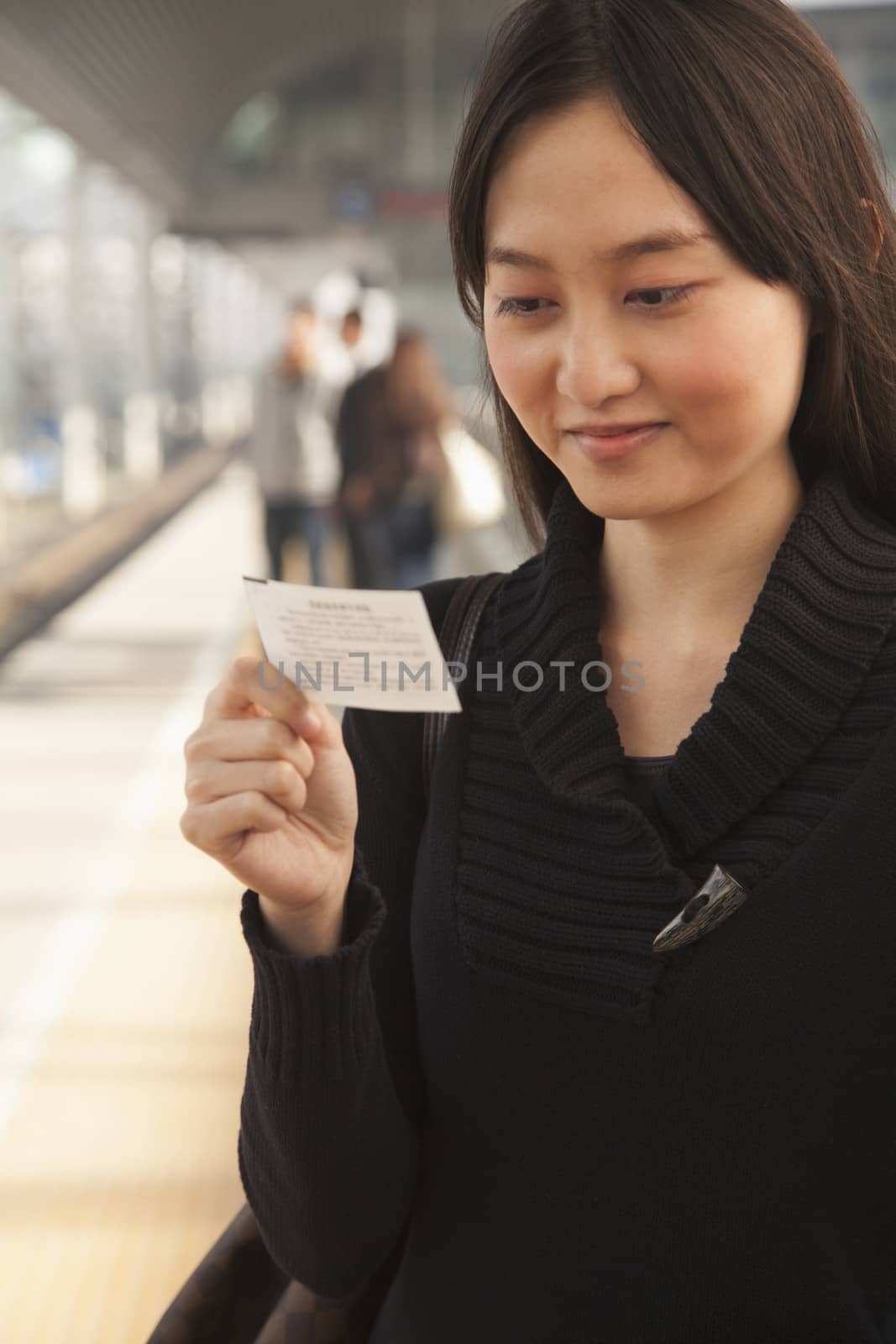 Young Woman Looking At Train Ticket on Railroad Platform