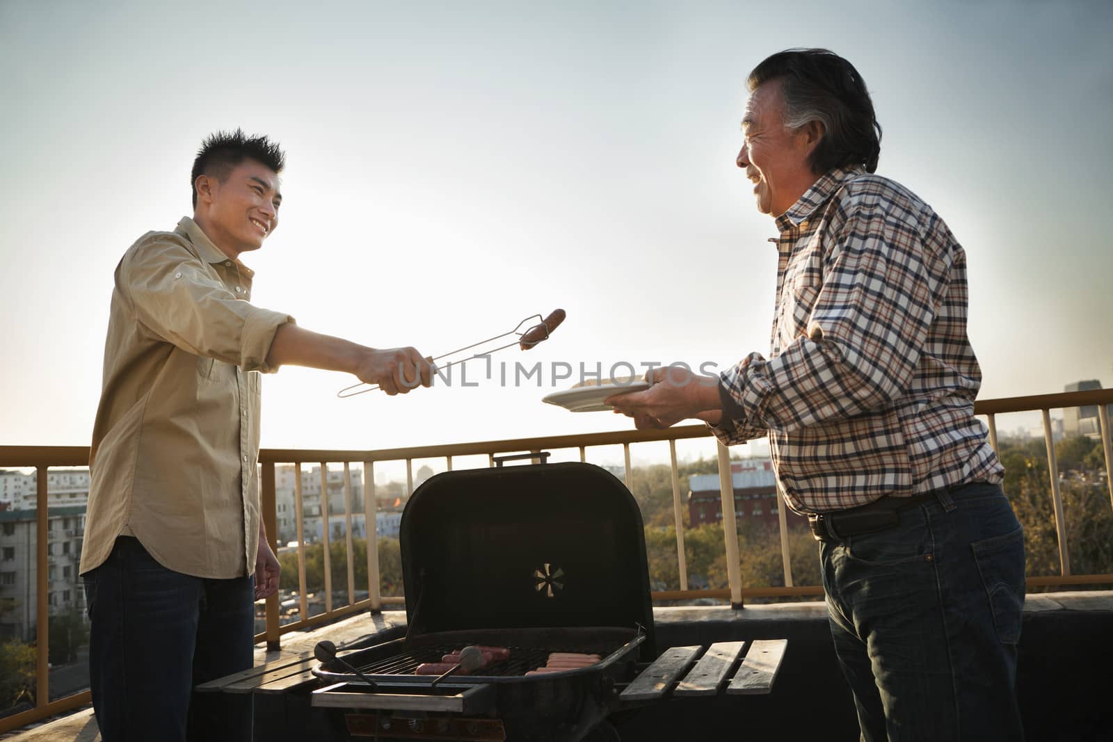 Son giving sausage to his father over the barbeque