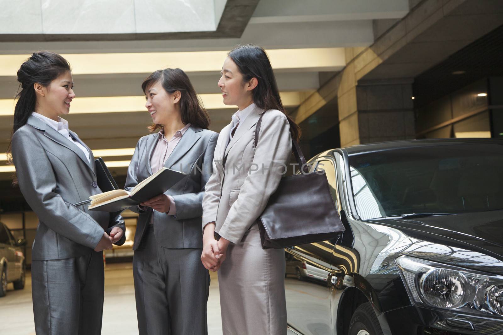 Three young businesswomen meeting and talking in parking garage by XiXinXing