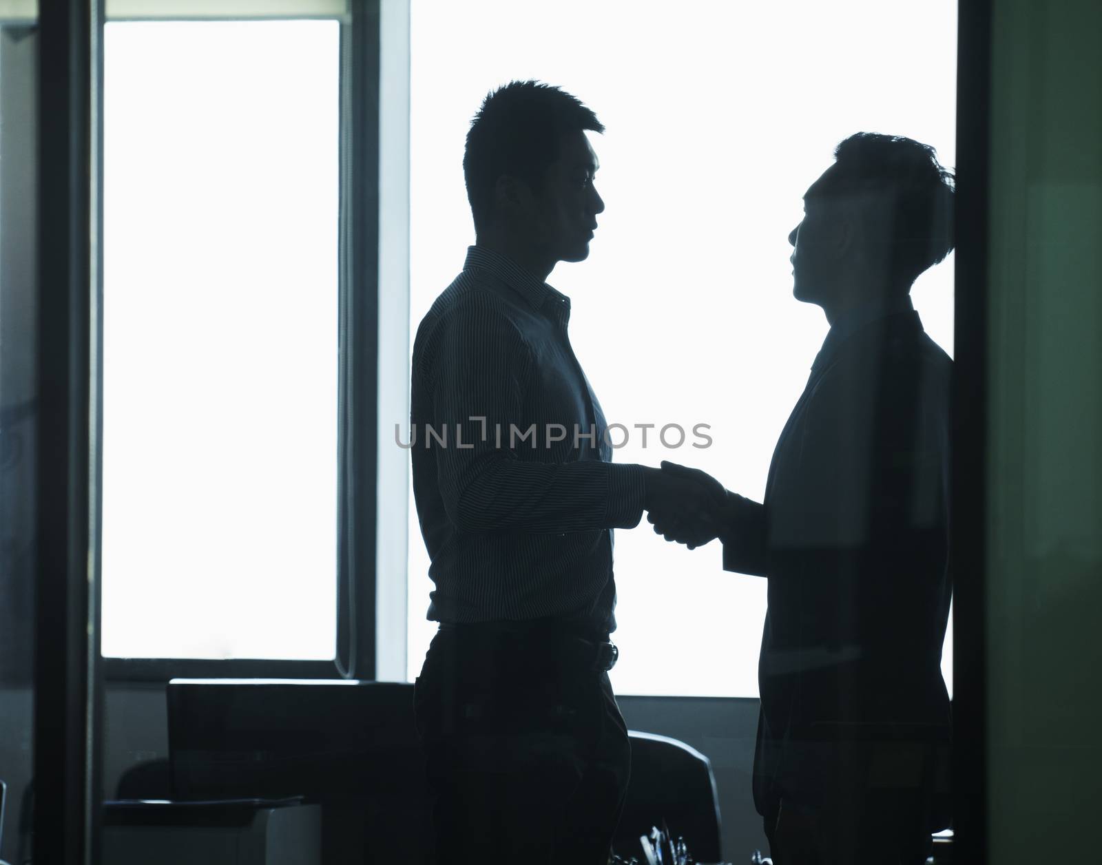 Businessmen shaking hands in office by XiXinXing