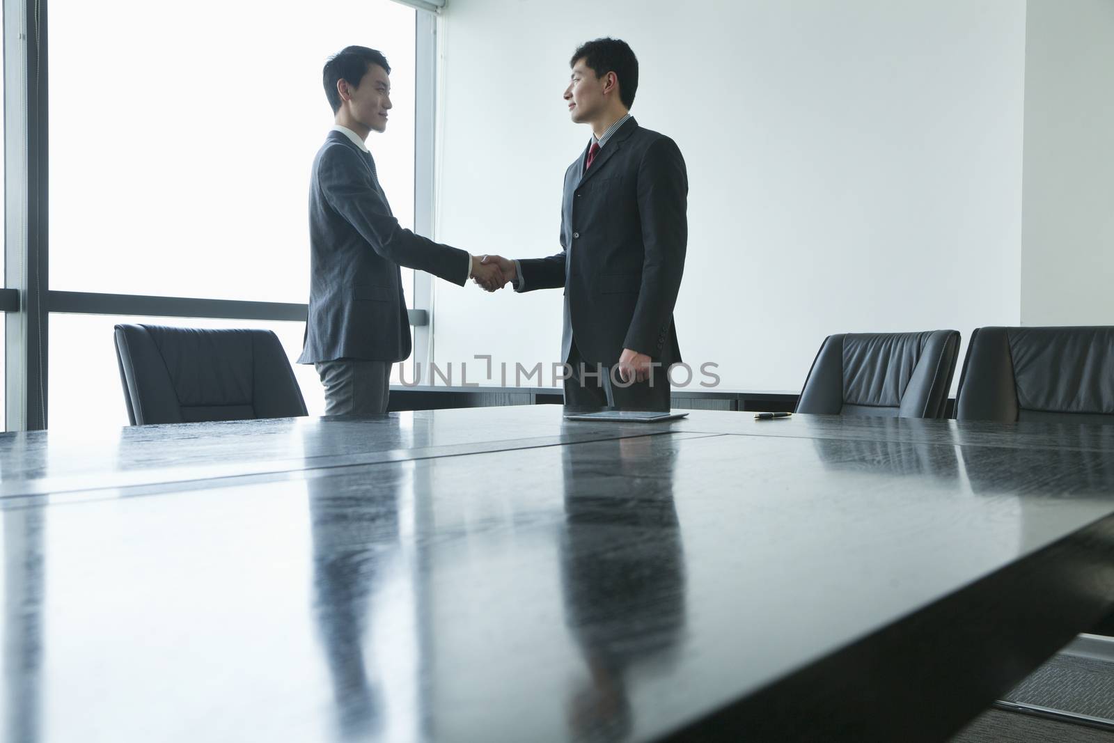 Businessmen shaking hands in meeting room by XiXinXing