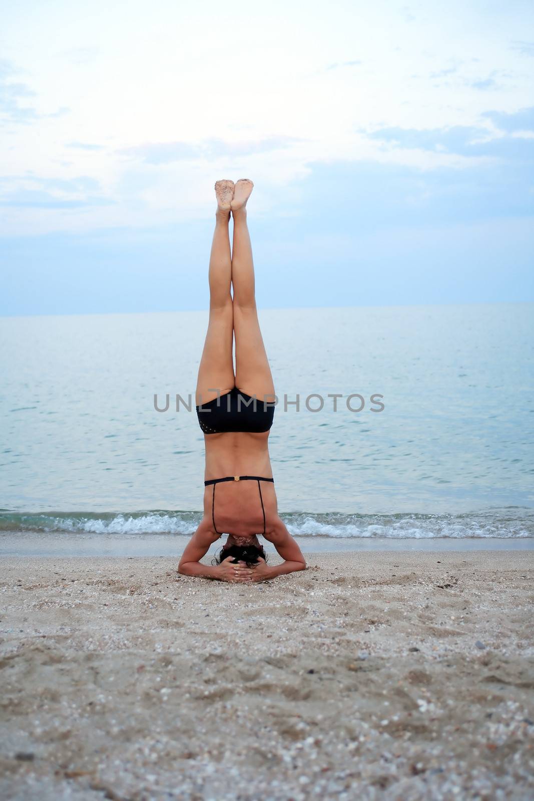 Svelte mature woman standing on her head near sea