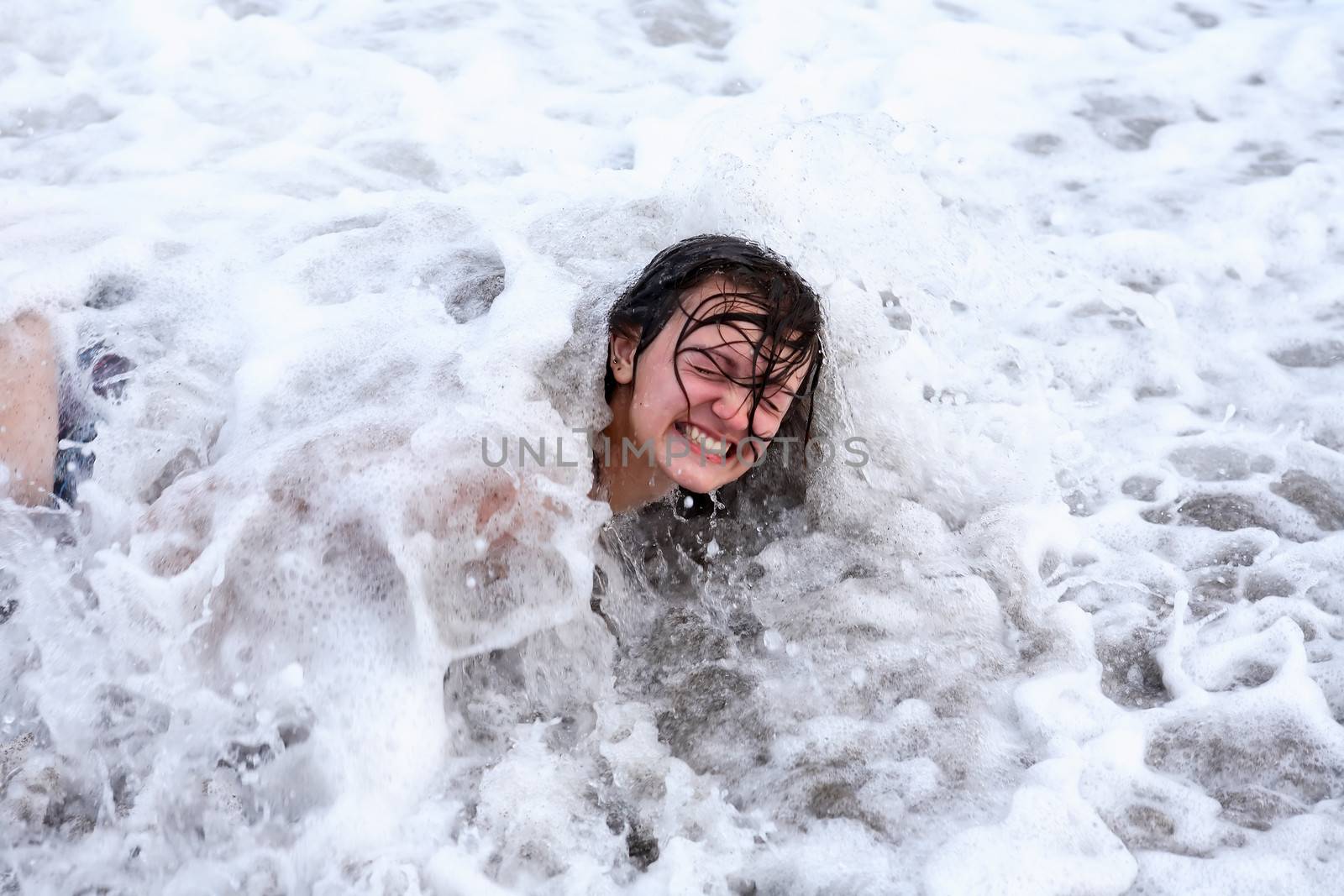 Portrait of smiling teenage girl in sea wave with foam