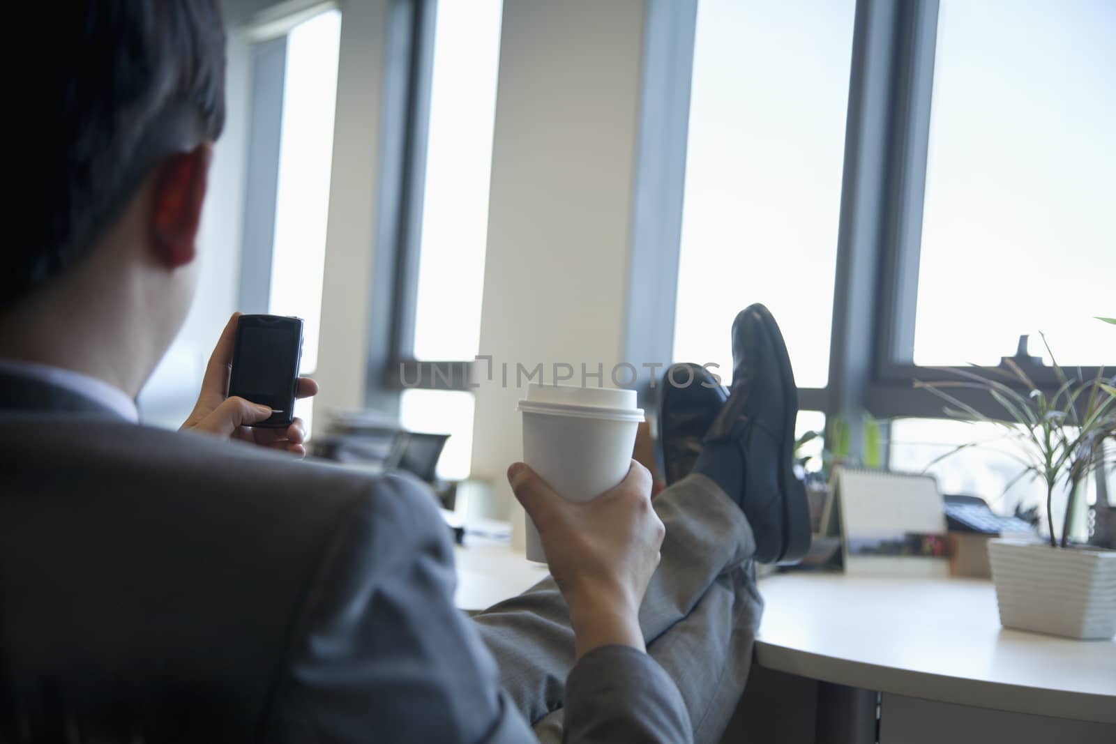 Businessman with feet up drinking coffee and text messaging