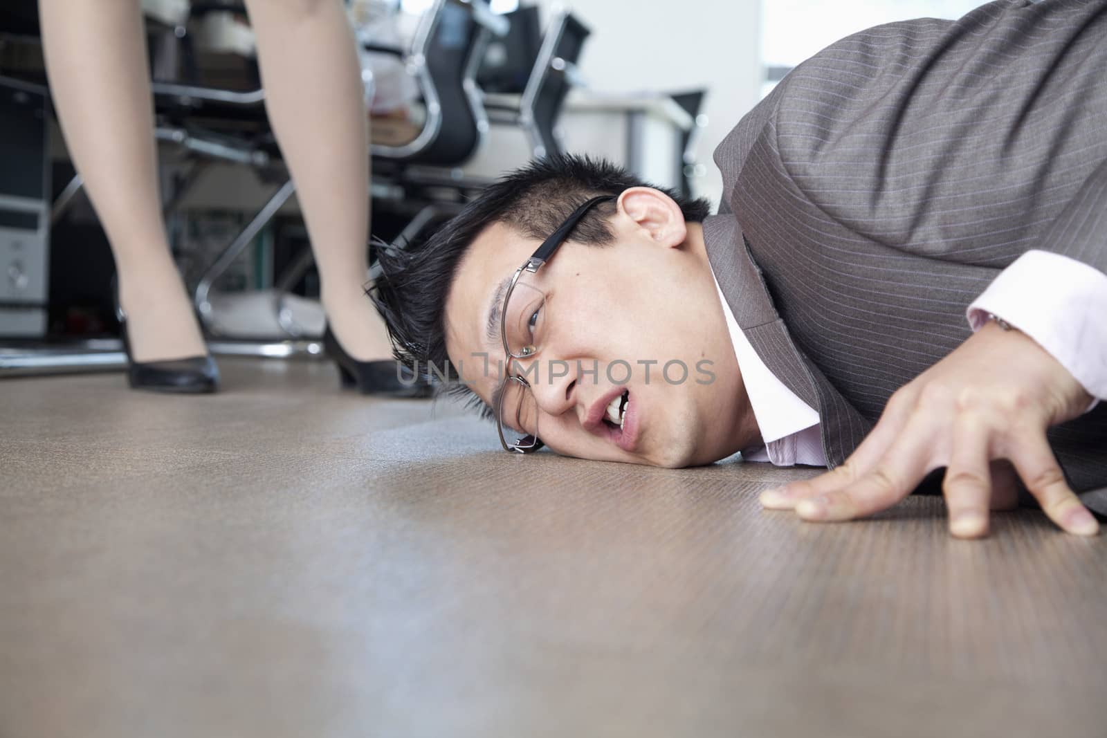 Businessman with face on the floor, coworker standing by him