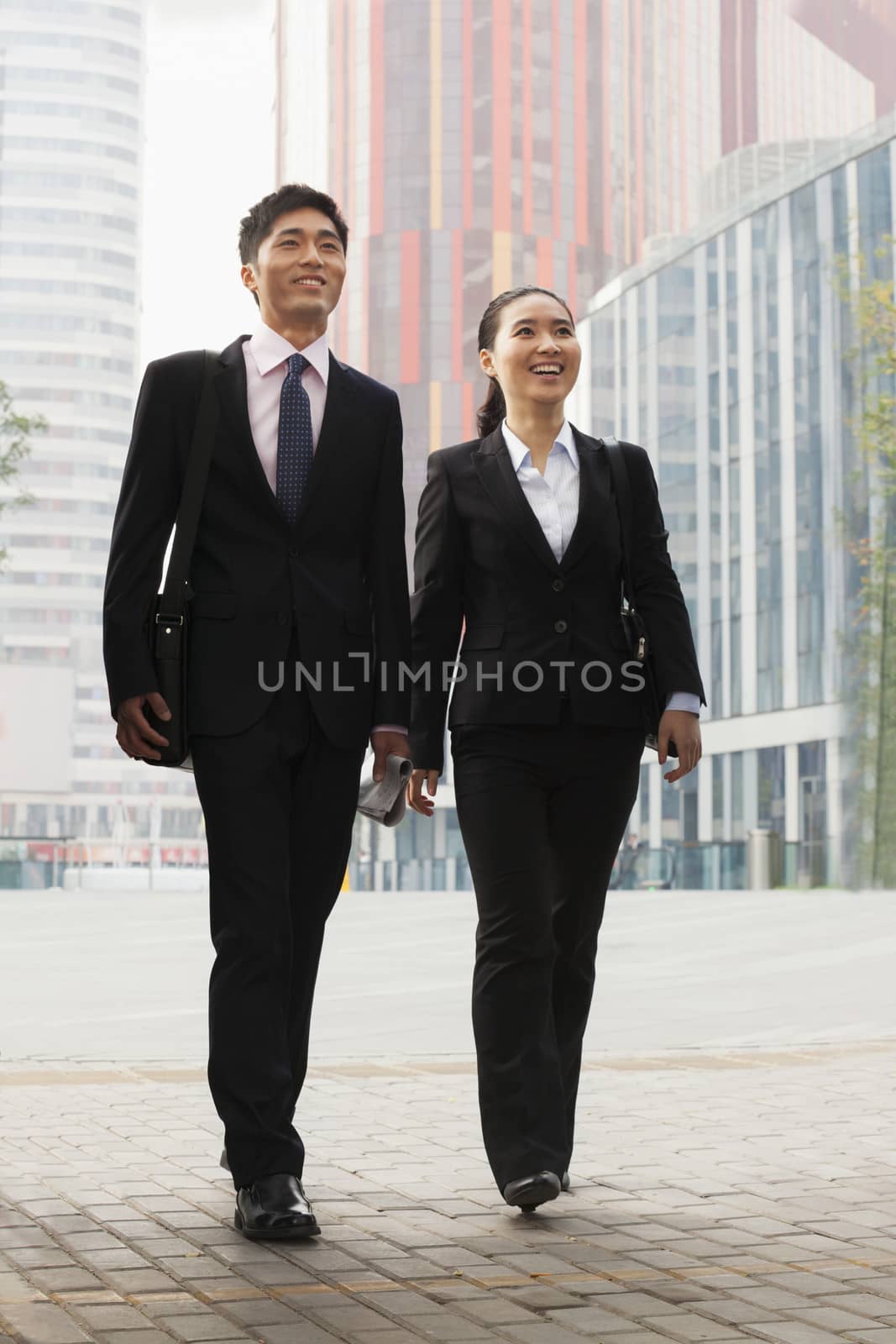  Two young business people walking outdoors, Beijing, China