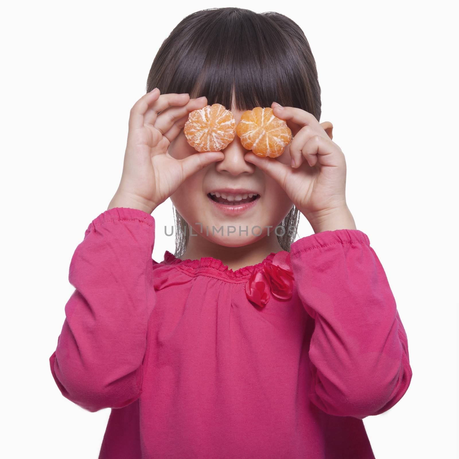 Little girl holding mandarins in front of her eyes, studio shot
