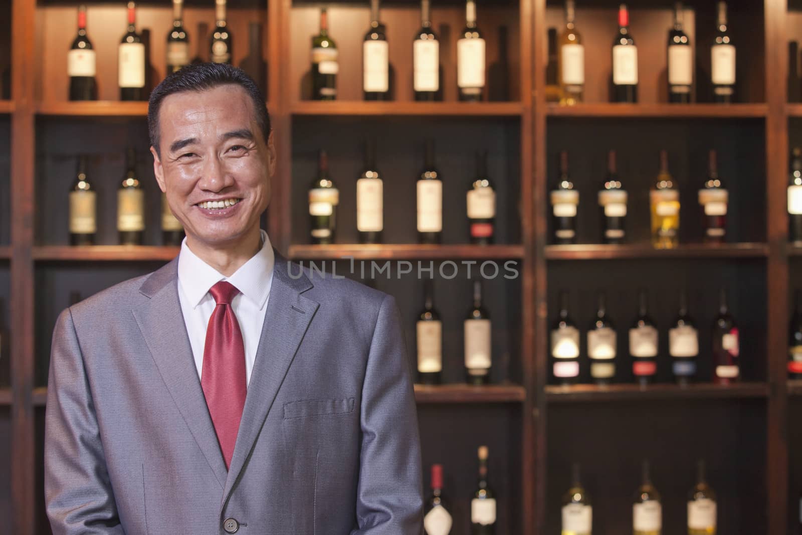 Smiling Businessman Standing by Wine Bottles, Portrait