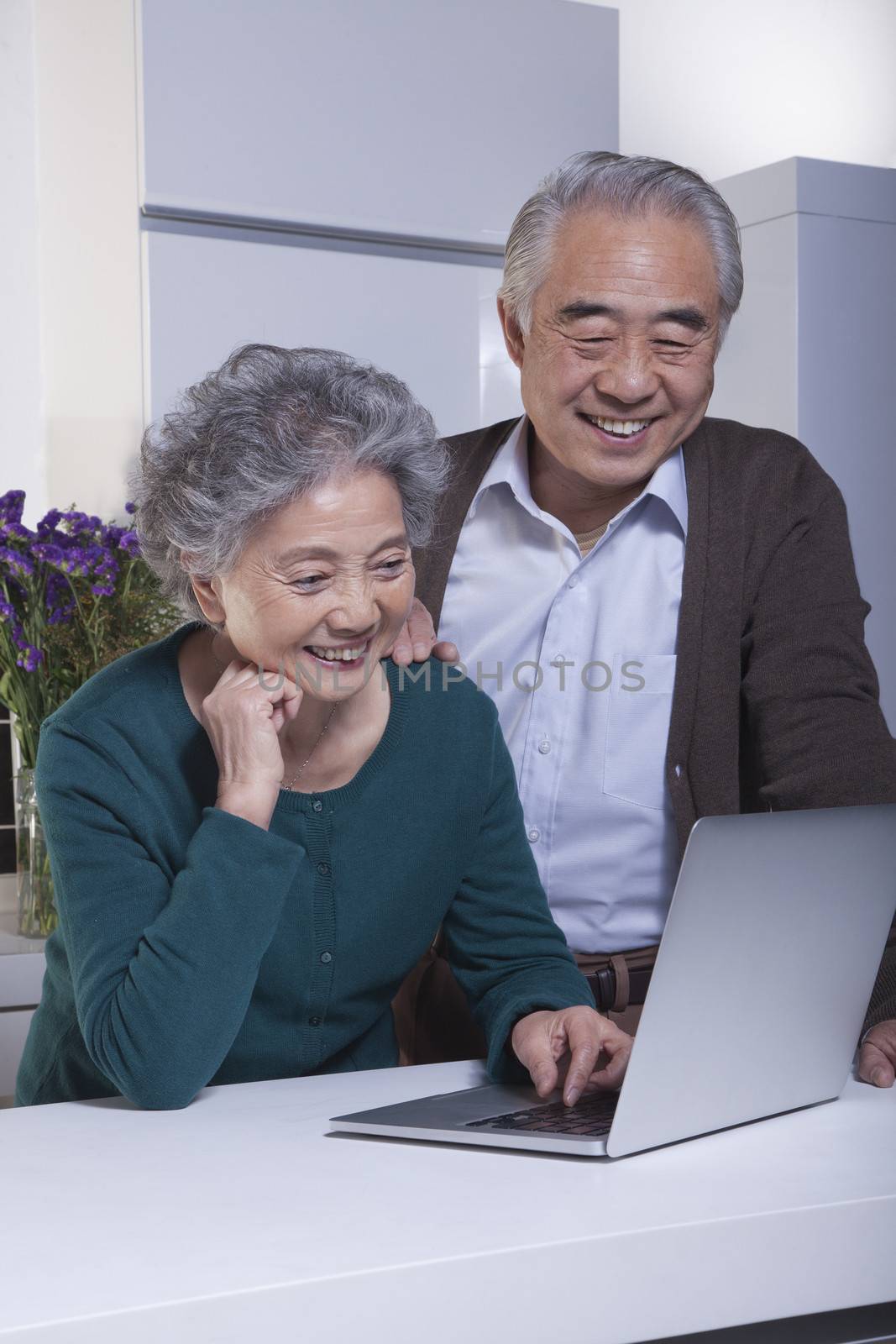 Mature Couple Looking at Laptop in the Kitchen  by XiXinXing