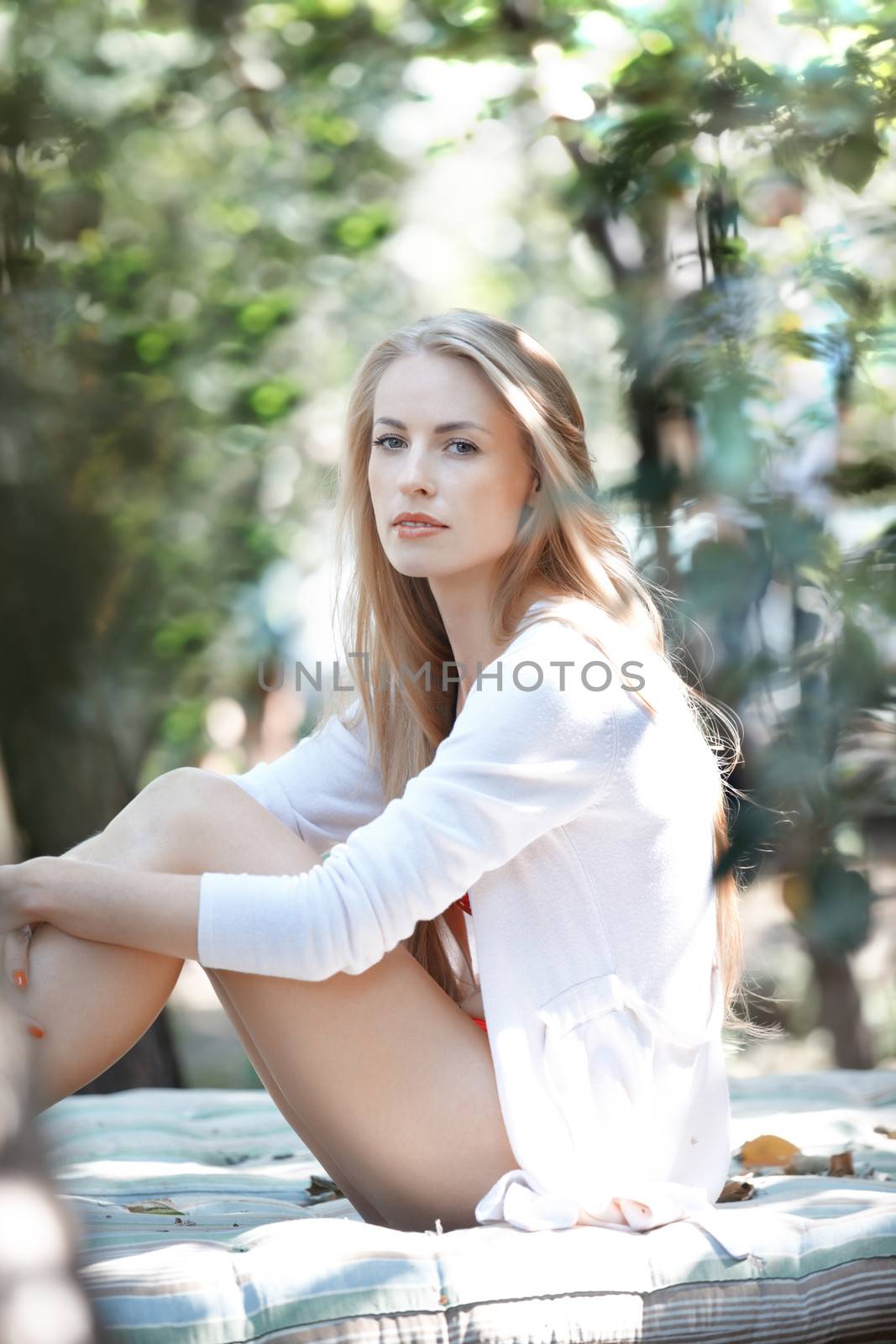 Beautiful lady in white shirt outdoors sitting on a bedding