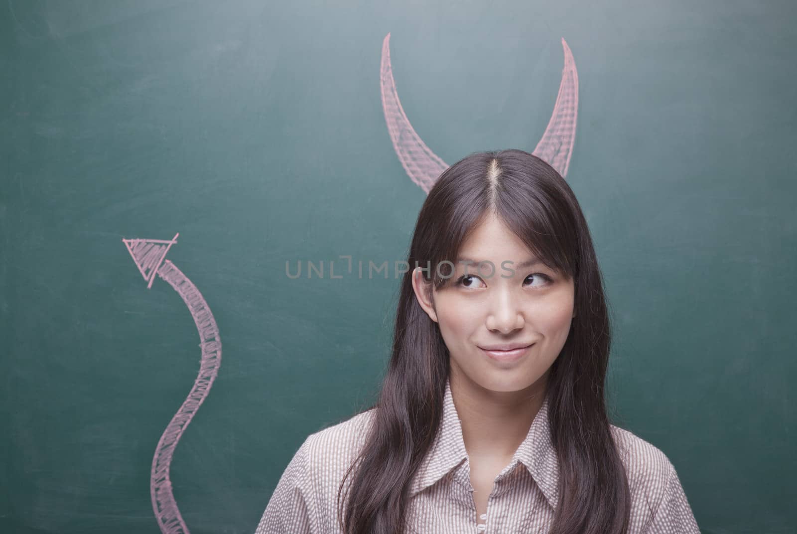 Young woman with devil horns and tail on blackboard