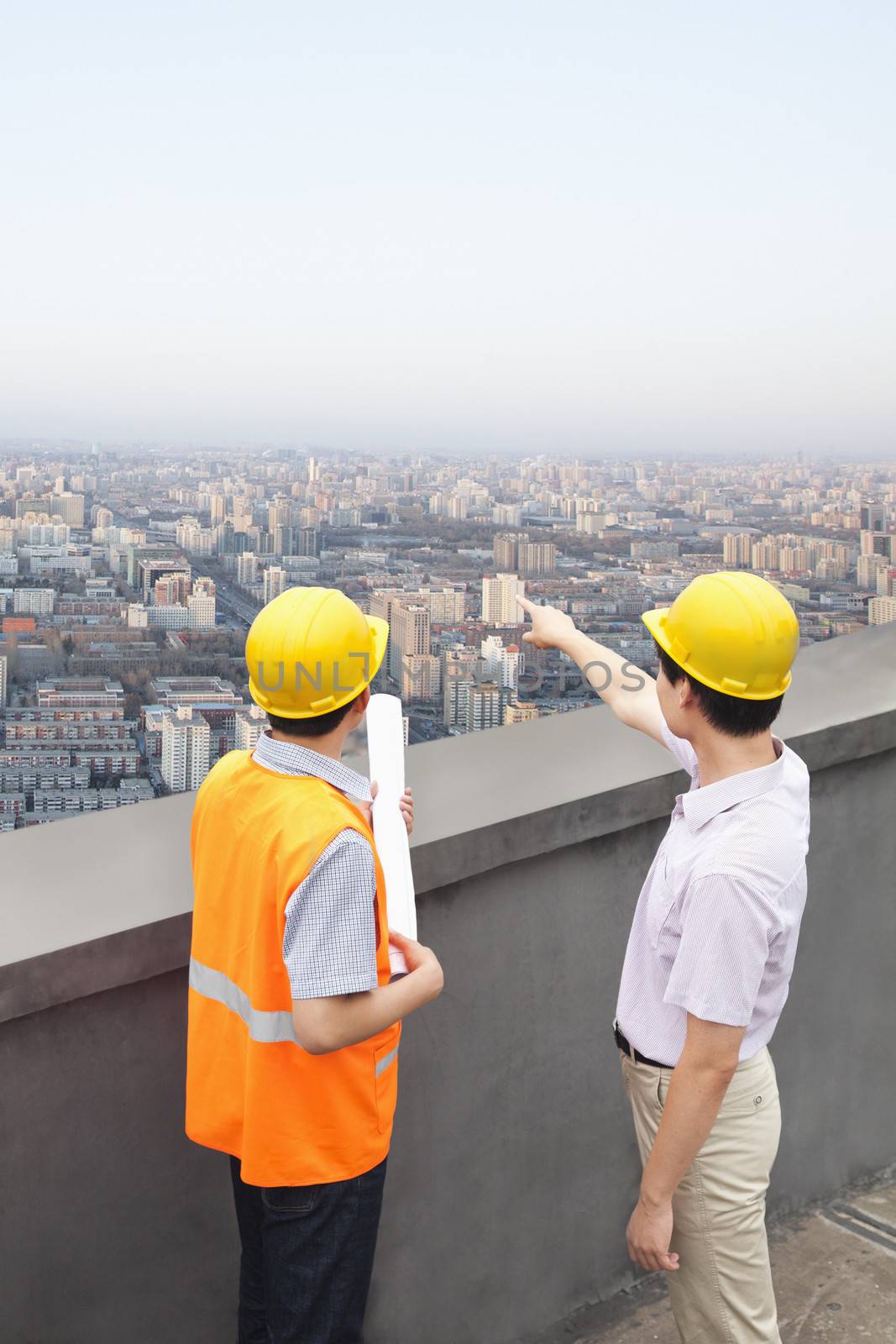 Architect And Construction Worker Talking On Rooftop by XiXinXing
