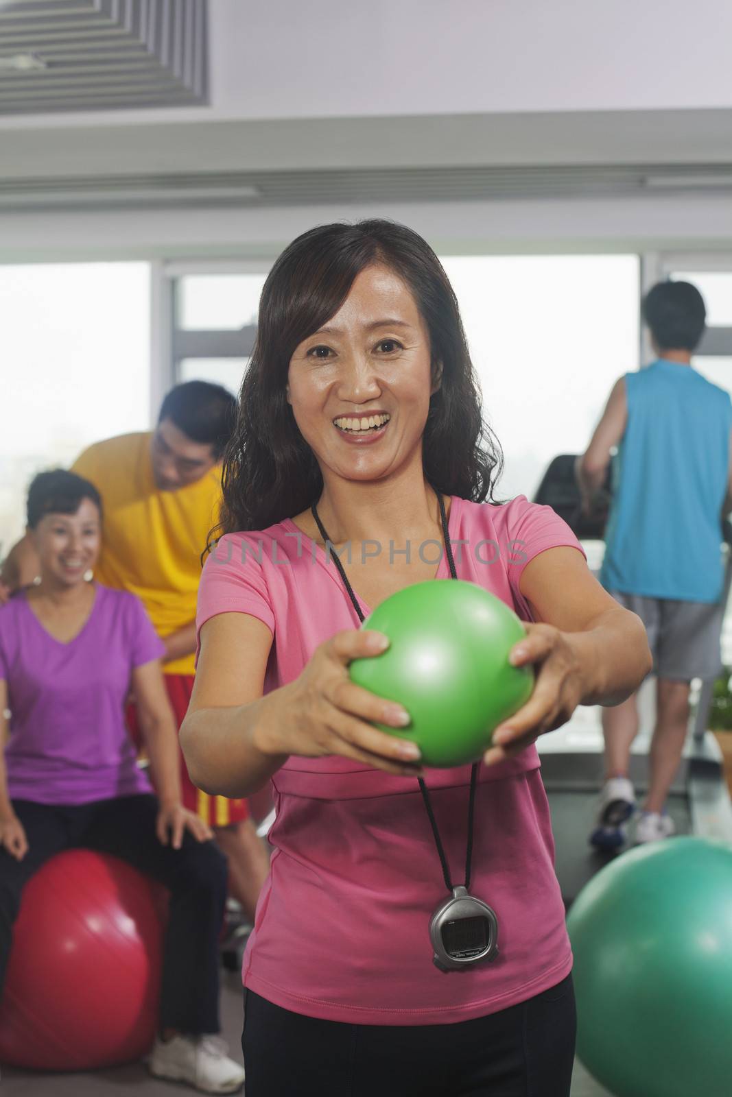 Woman holding ball on foreground, people working out in the gym on the background