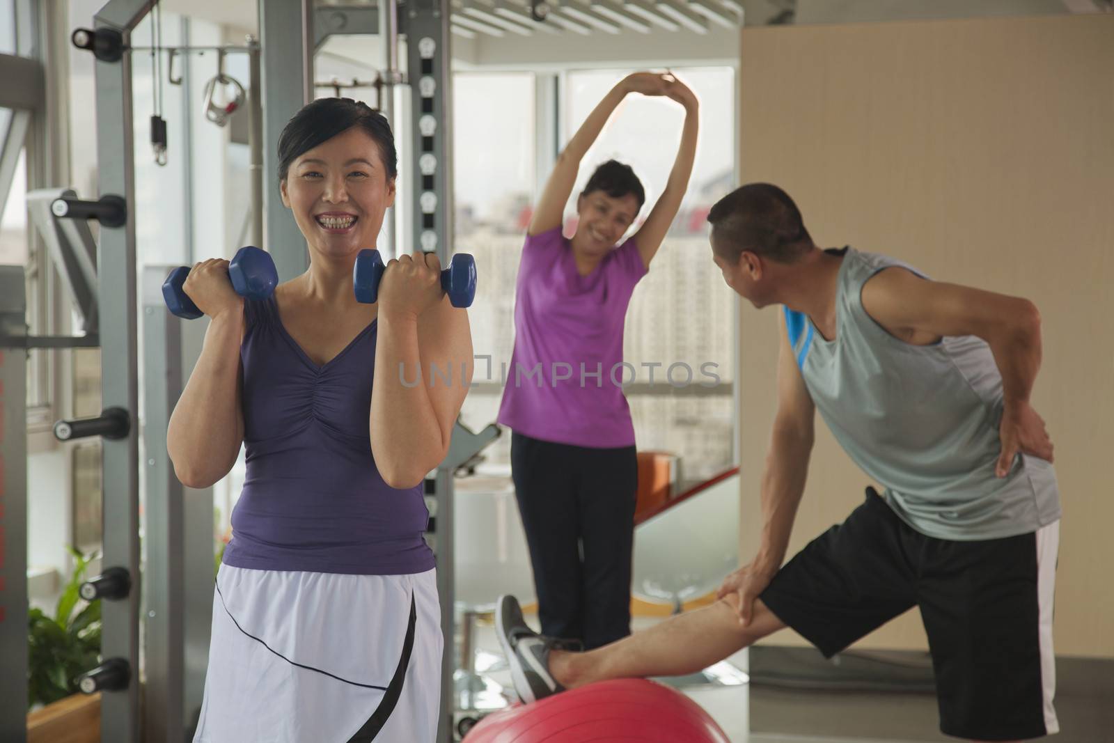 mature woman lifting weights in the foreground, people exercising in the background by XiXinXing