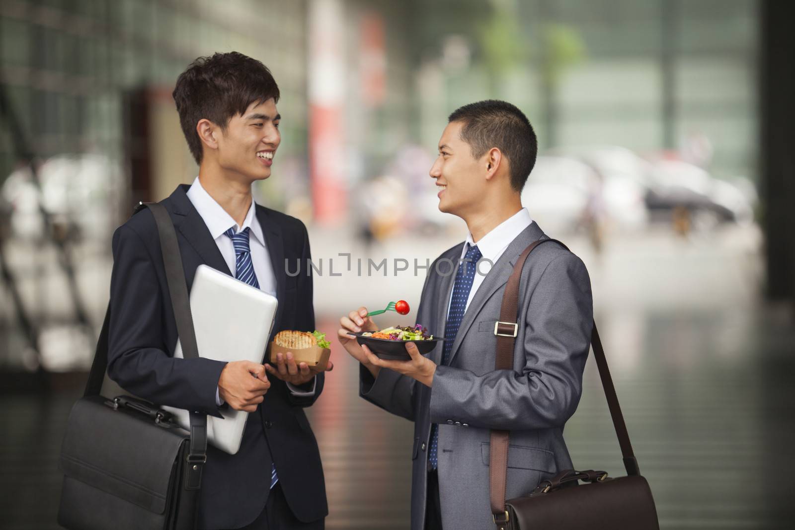 Two young businessmen talking and having a lunch outdoor by XiXinXing