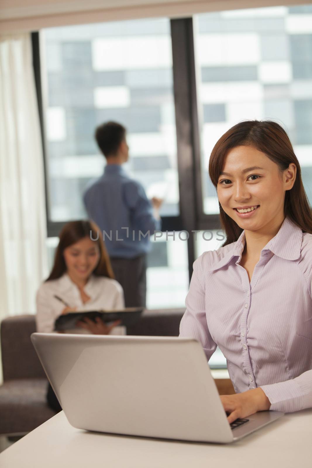 Businesswoman working on her laptop, coworkers on the background