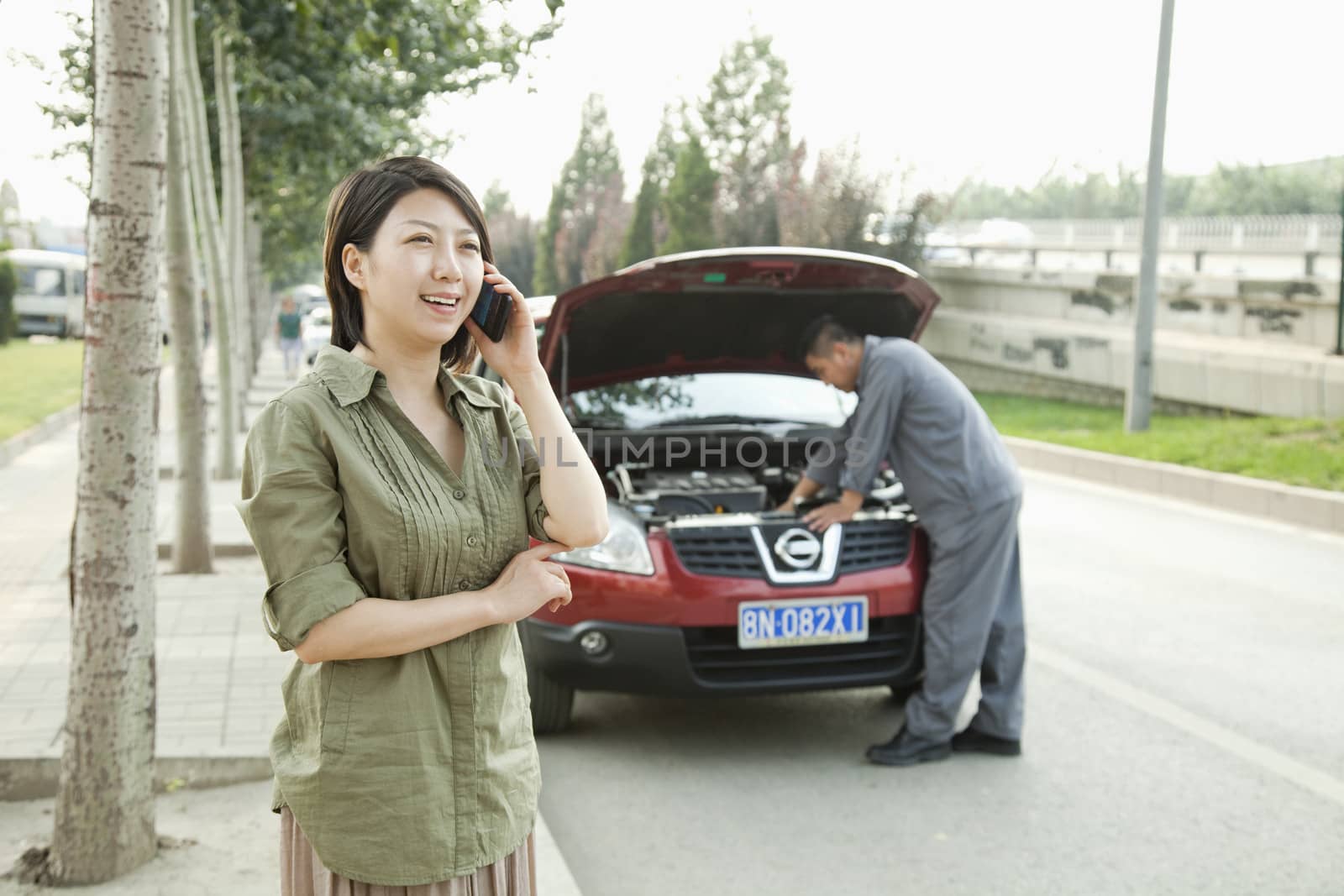 Woman Talking on Phone While Mechanic Fixes Her Car by XiXinXing