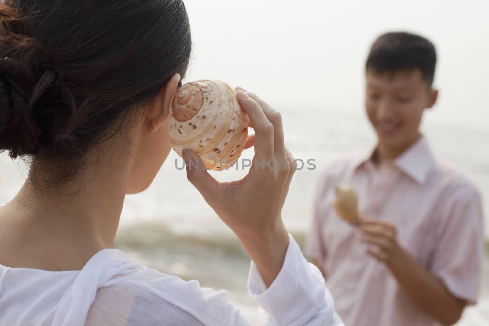 Young couple looking at seashells, holding shell to ear 