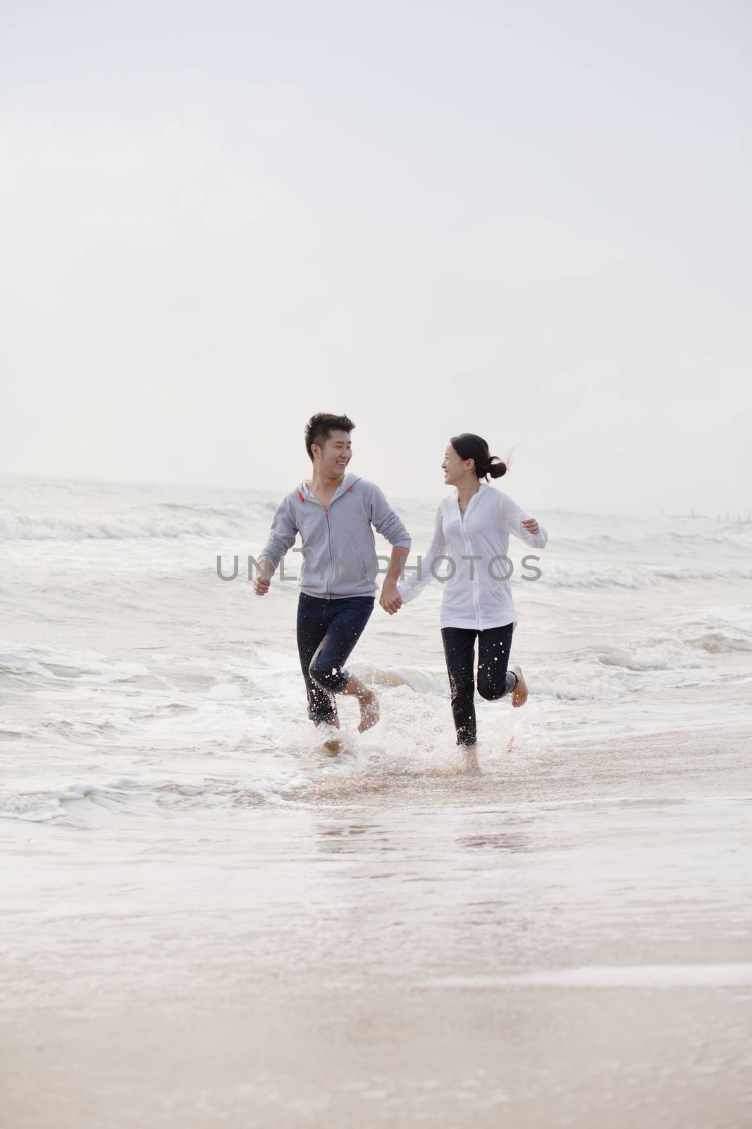 Young couple holding hands running by the waters edge on the beach, China