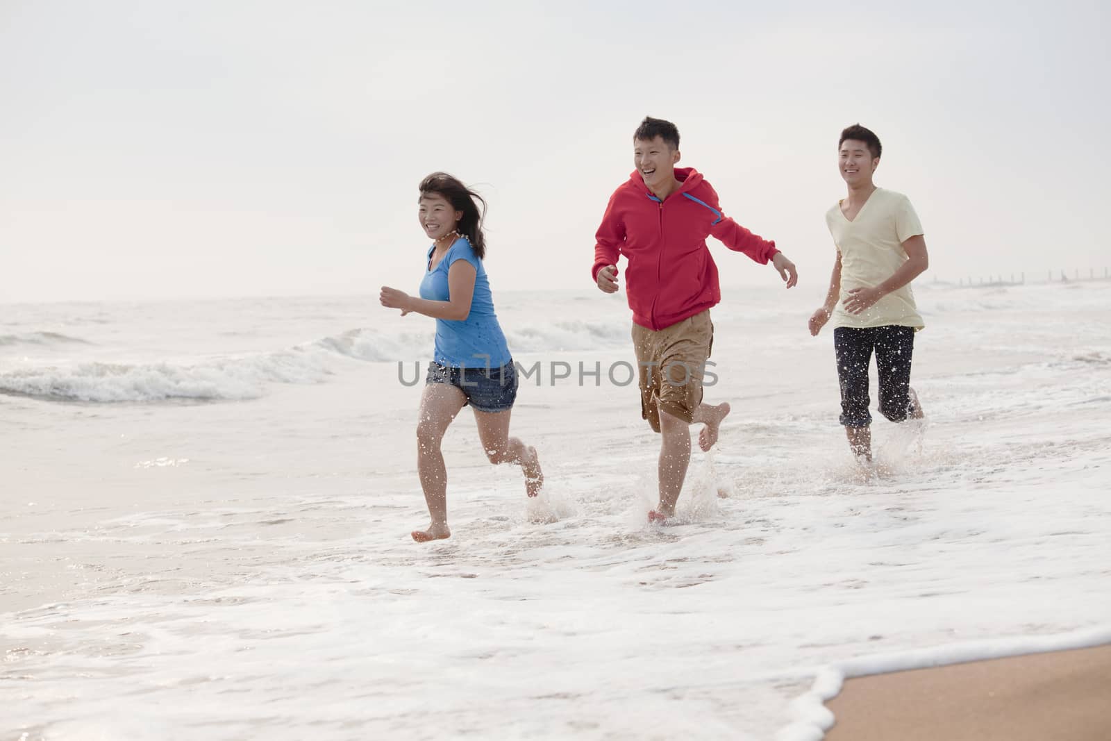 Three friends running on the beach by the waters edge, China by XiXinXing