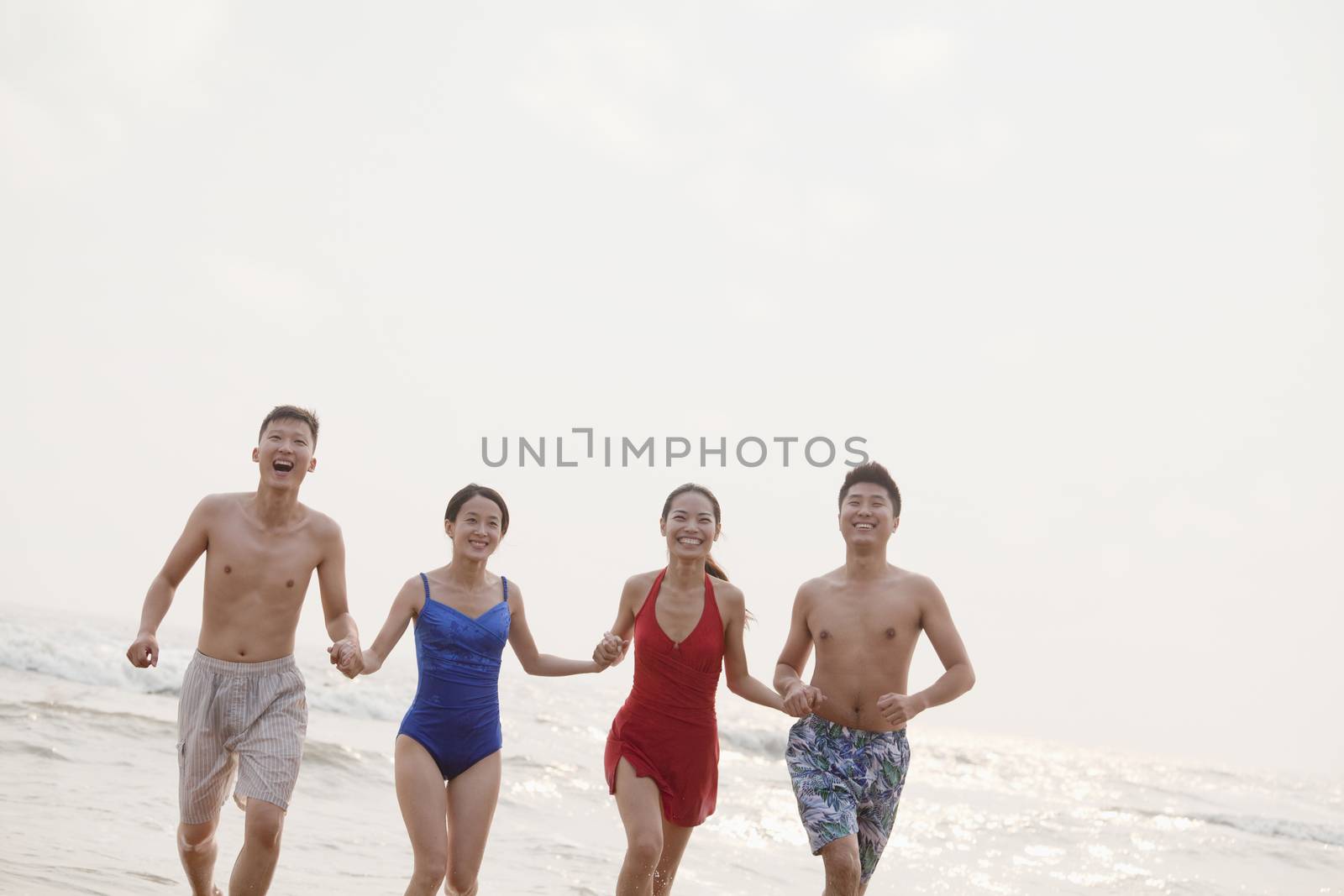 Four friends running into the water on a sandy beach