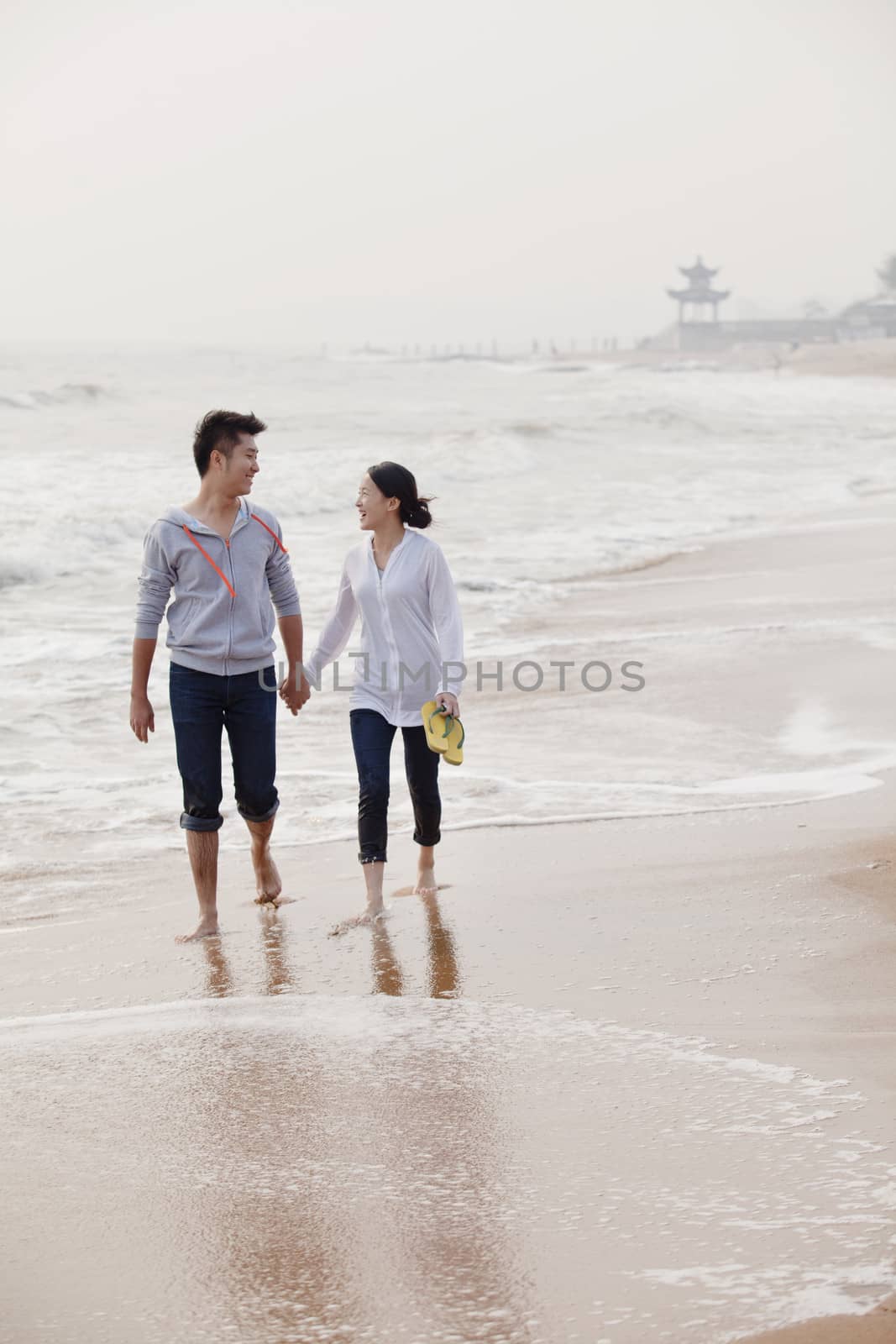 Young couple walking by the waters edge on the beach, China by XiXinXing