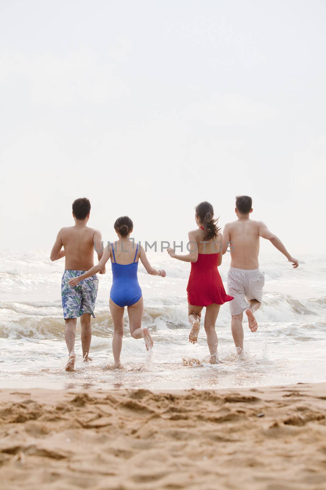 Four friends running into the water on a sandy beach