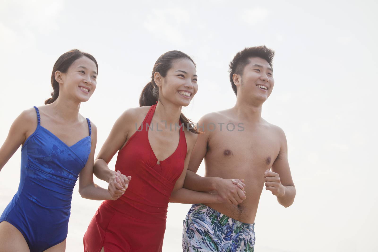 Three friends holding hands and smiling on the beach