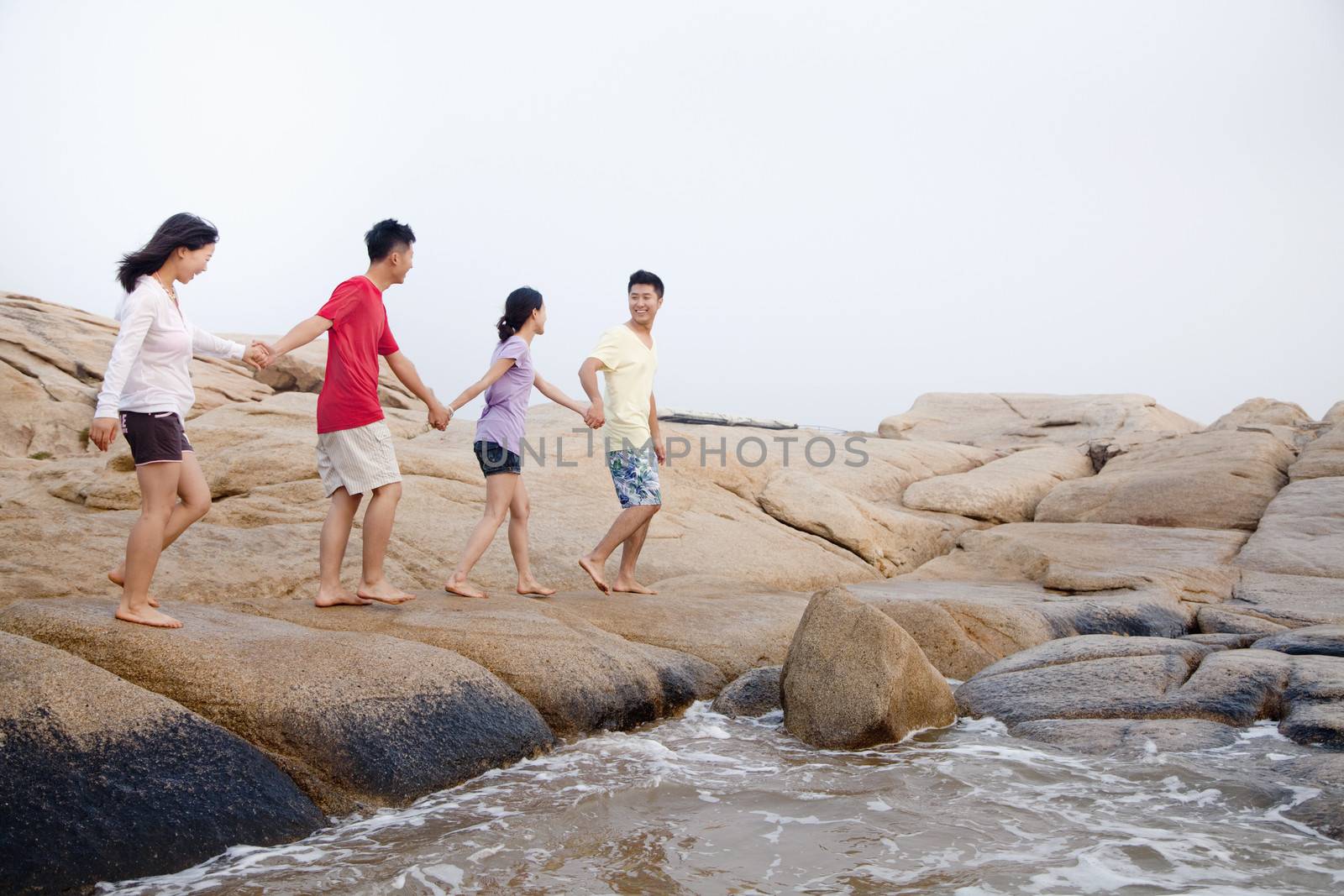 Four friends walking over rocks by the sea