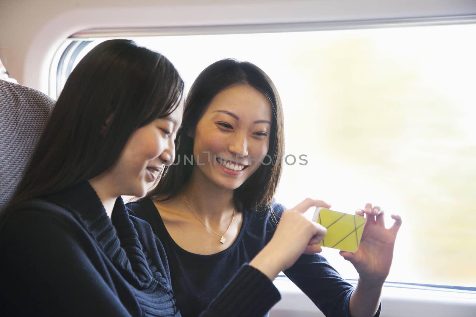 Two Women Looking At Mobile Phone on a Train by XiXinXing