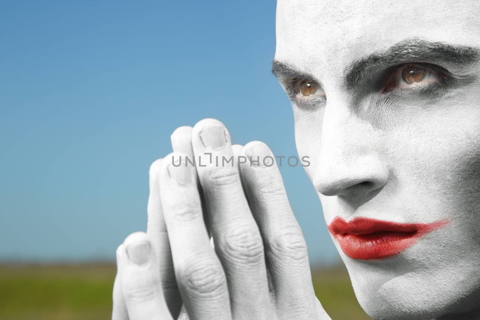 Human with clown makeup praying outdoors. Vibrant colors 