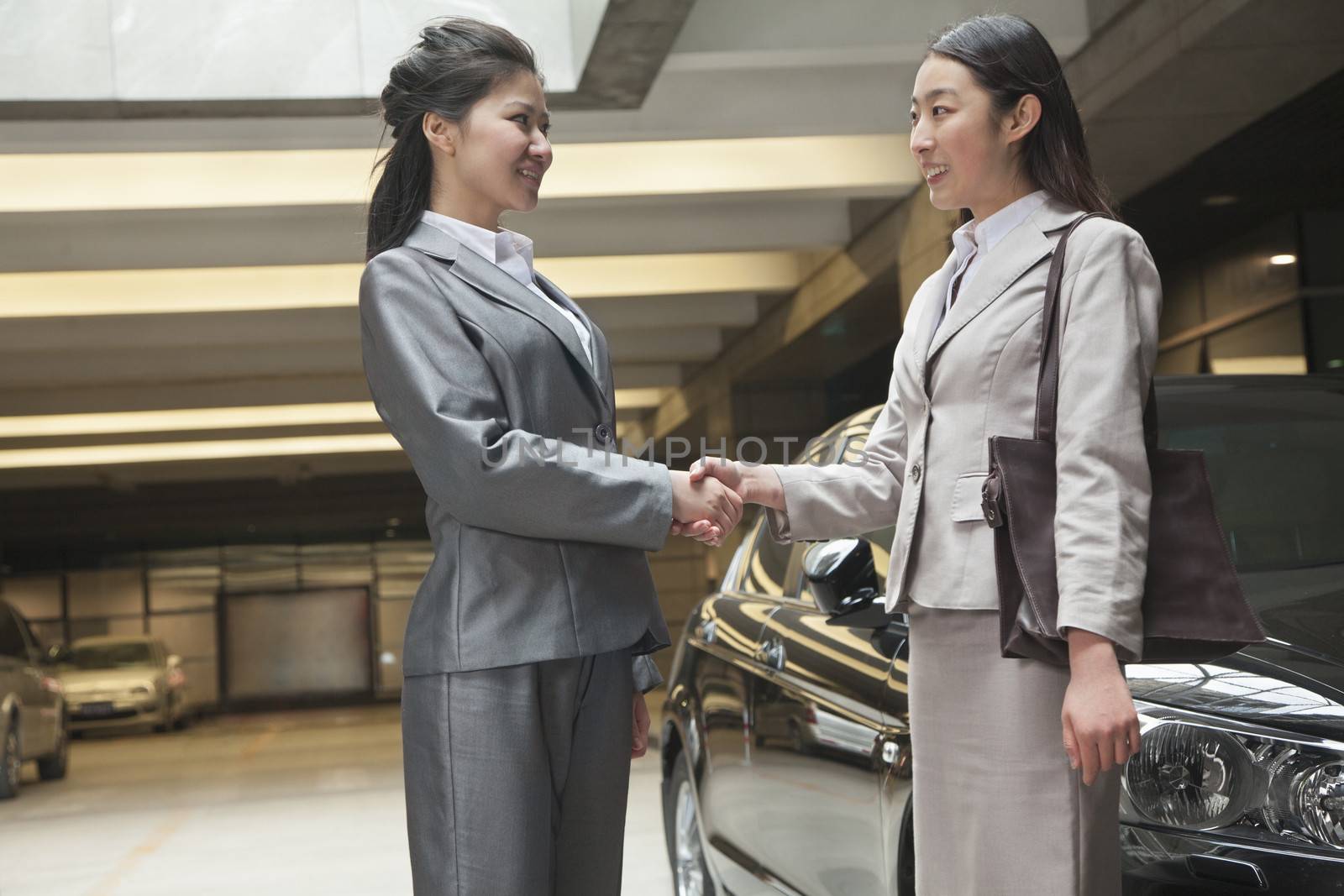 Two young businesswomen shaking hands in parking garage by XiXinXing
