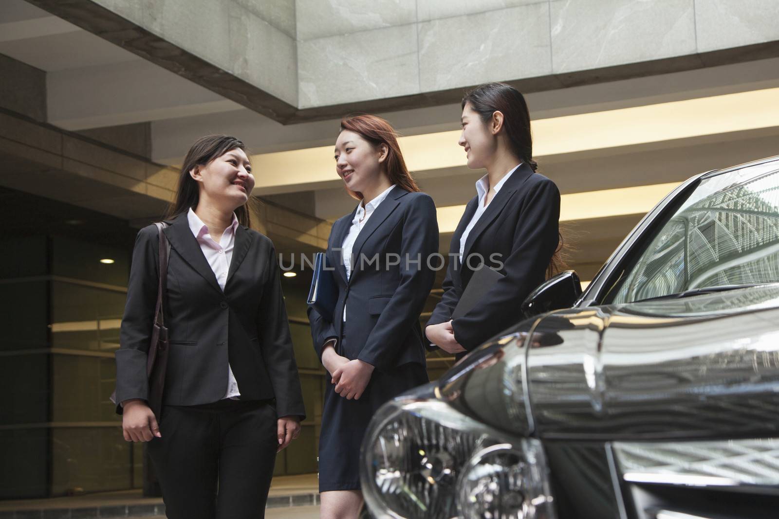 Three young businesswomen meeting and talking in parking garage by XiXinXing