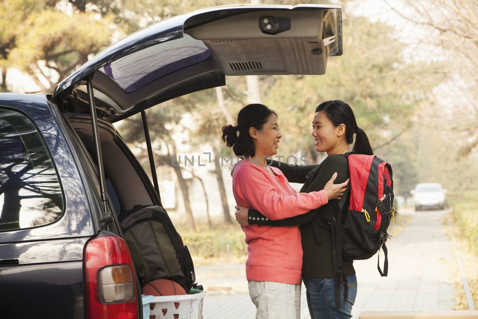 Mother and daughter embracing behind car on college campus by XiXinXing