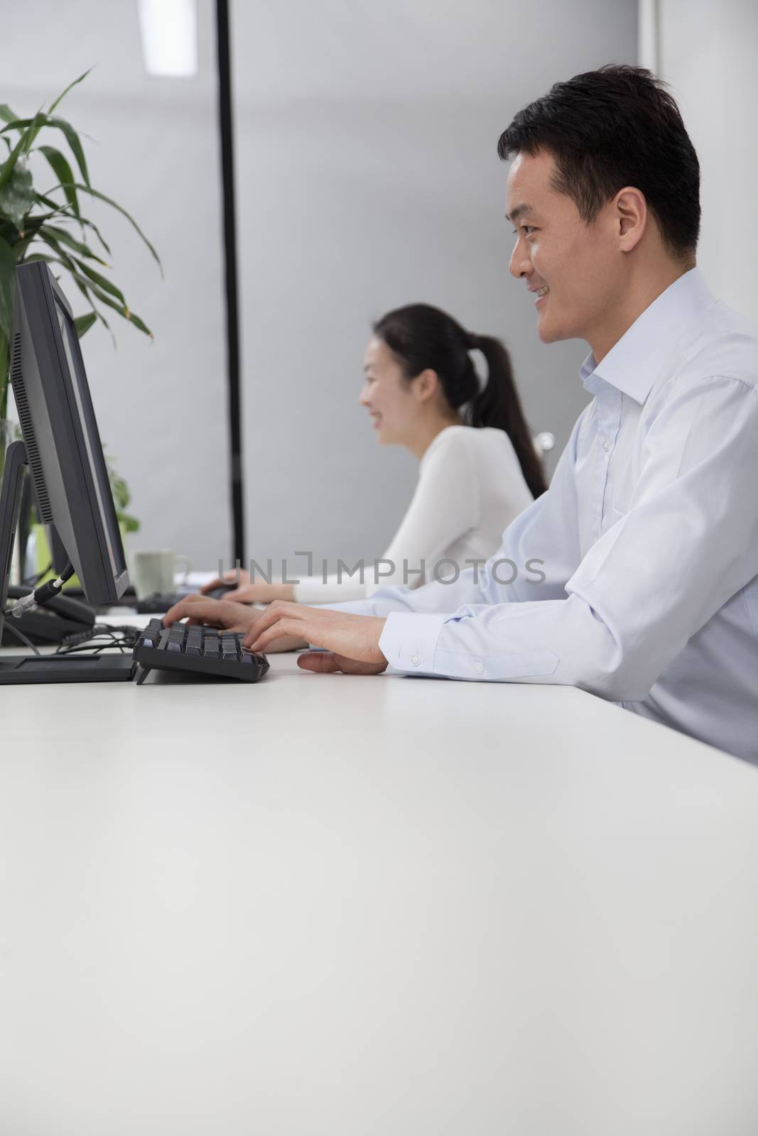 Happy coworkers working on their computers in the office by XiXinXing