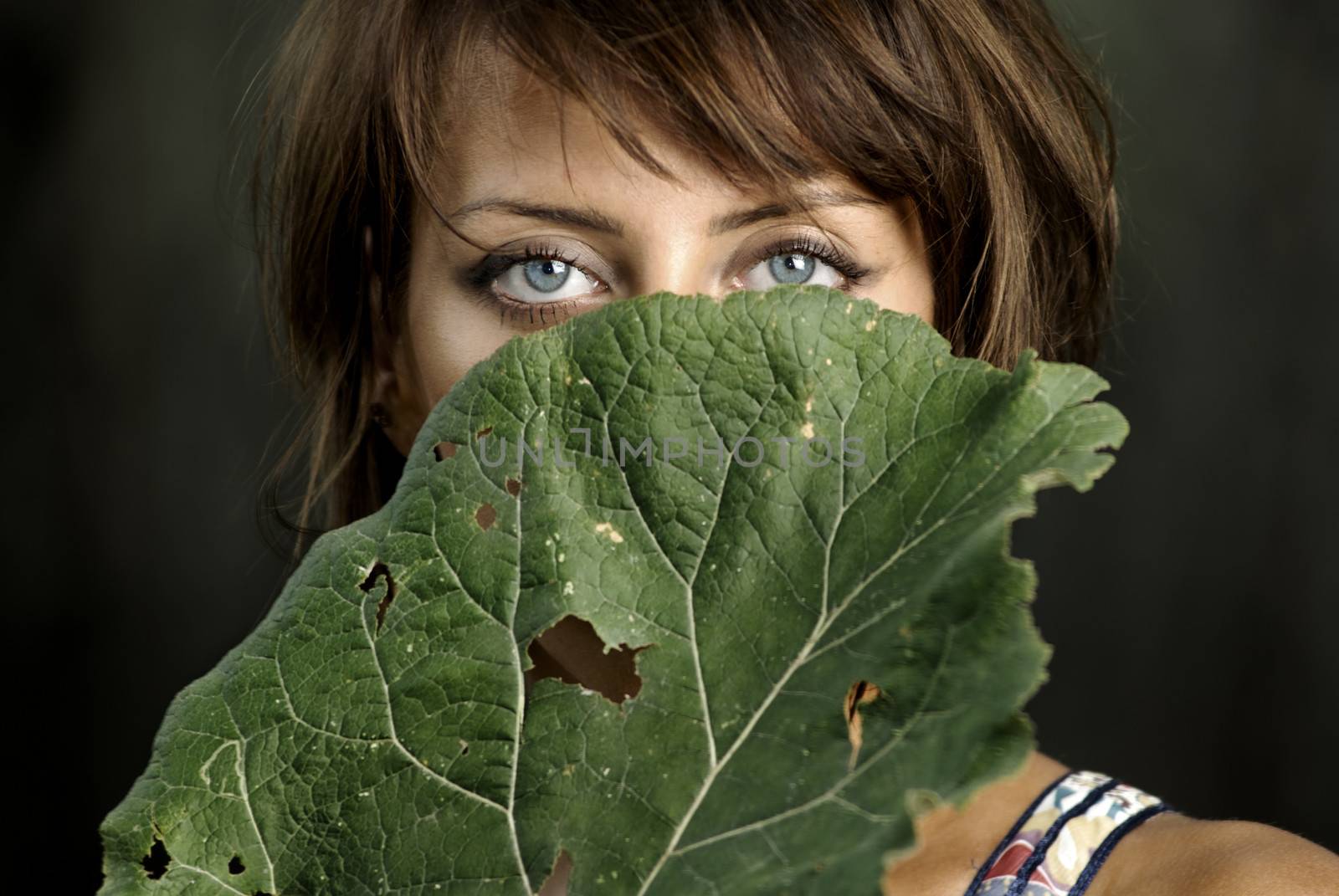 Half-face of the beautiful lady hidden by the burdock leaf