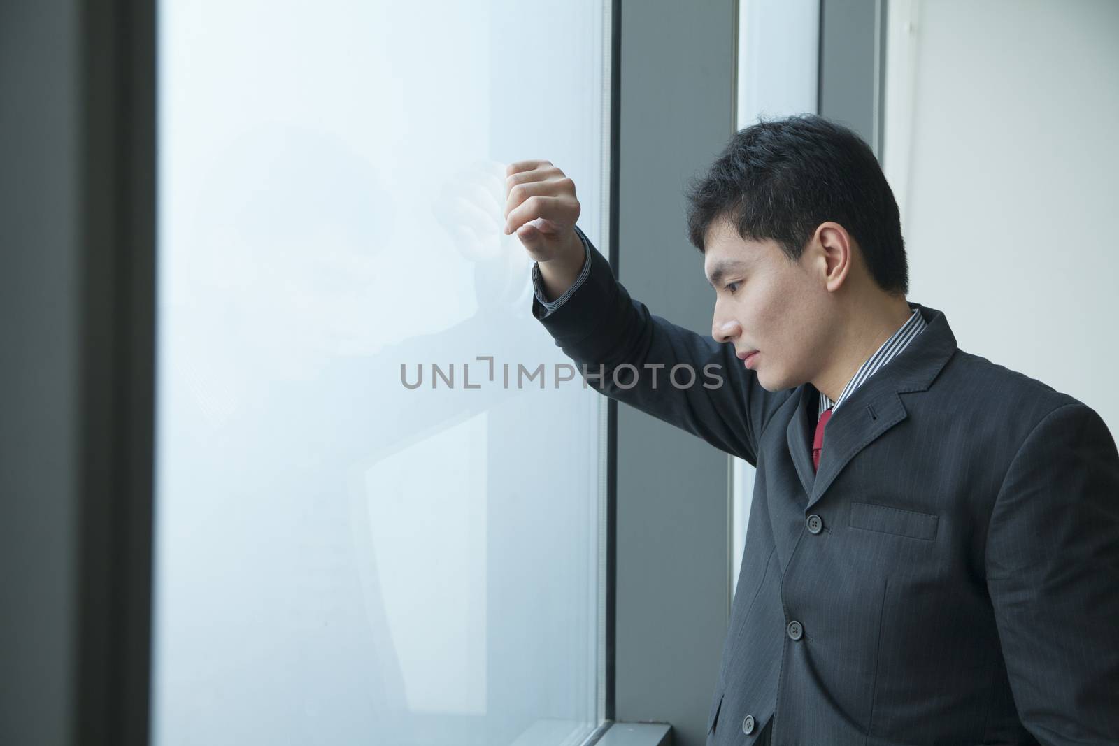 Businessman looking through window in office by XiXinXing