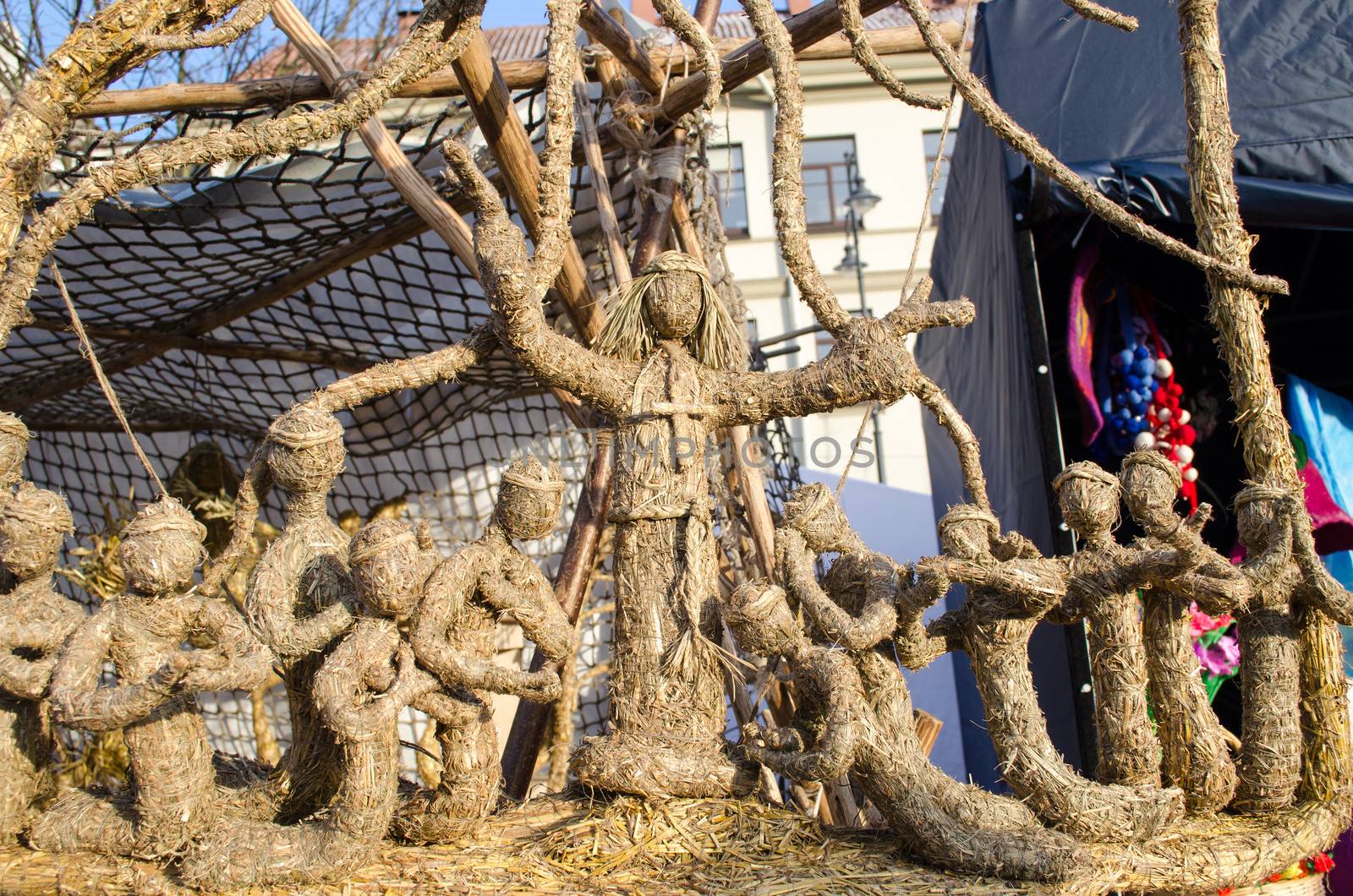 priest god jesus with cross on chest and prayers figures decorations kneel against him made of straw hay. exhibition in outdoor street spring fair market.